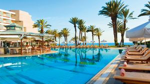 Großer Außenpool mit zahlreichen Liegen, Palmen und einer stilvollen Poolbar direkt am Wasser.