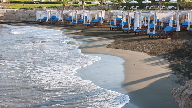 Eleganter Strandabschnitt mit weißen Baldachinliegen und blauen Polstern direkt am Wasser – ideal für erholsame Stunden mit Meeresrauschen.