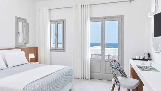 Helles und stilvolles Doppelzimmer im Costa Grand Resort & Spa – modernes Design in Weiß und Grau mit gemütlichem Bett, Arbeitsbereich und direktem Meerblick durch große Fenster.