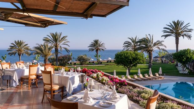 Genießen Sie ein stilvolles Abendessen auf der Terrasse mit Blick auf Palmen, Pool und das weite Meer – perfekt zum Sonnenuntergang.