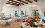 Elegantes Hotelrestaurant mit mediterranem Flair, hellen Bögen und Meerblick – liebevoll gedeckte Tische mit blauen Akzenten und kunstvoll arrangiertes Obstbuffet sorgen für ein stilvolles Ambiente.