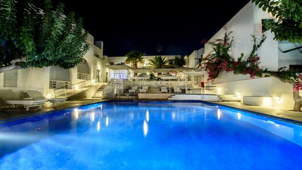 Stimmungsvoll beleuchteter Hotelpool bei Nacht – weiße Gebäude im Kykladenstil, umgeben von Palmen, Bougainvillea und gemütlichen Liegen.