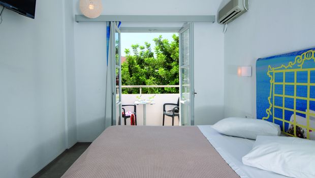 Helles Hotelzimmer mit Doppelbett, Klimaanlage und Zugang zu einem Balkon mit Sitzgelegenheit und Blick ins Grüne – ideal zum Entspannen.