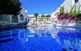 Großer Außenpool eines mediterranen Hotels mit Sonnenliegen, weißen Gebäuden, Palmen und blühender Bougainvillea – perfekte Kulisse für entspannte Urlaubsmomente.