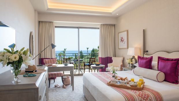 Helles, stilvoll eingerichtetes Zimmer mit Meerblick und liebevoll angerichtetem Frühstück auf dem Bett.