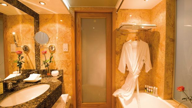 Elegantes Badezimmer in warmen Marmortönen mit großer Spiegelwand, Badewanne, Granitwaschtisch und gemütlichem Bademantel.