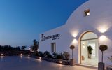 Beleuchteter Hoteleingang des Costa Grand Resort & Spa am Abend – modernes, weißes Gebäude im Kykladenstil mit stilvoller Außenbeleuchtung und mediterraner Bepflanzung.