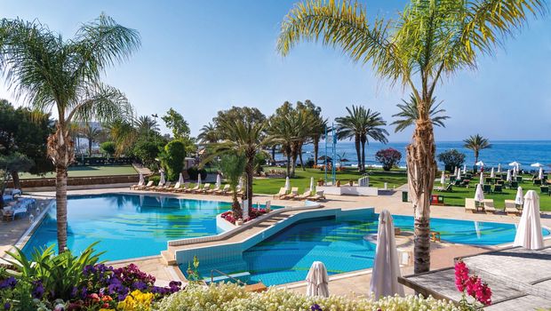 Luxuriöser Pool mit Meerblick, umgeben von Palmen, Blumen und Liegen – perfekte Wohlfühloase.