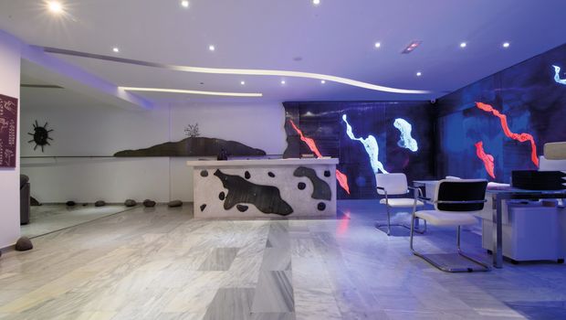 Modern gestalteter Rezeptionsbereich mit kunstvoll beleuchteter Wand in Blau-, Rot- und Weißtönen sowie stilvollen Sitzmöglichkeiten – Empfang mit kreativem Flair.