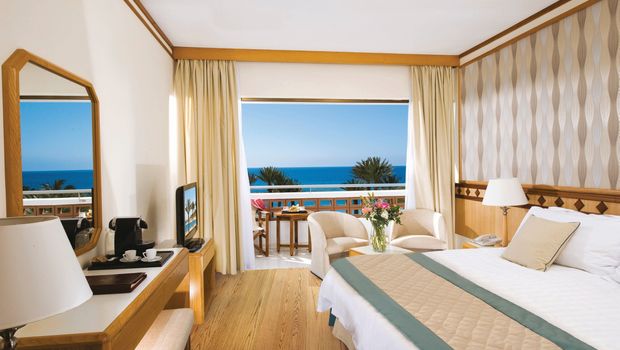 Helles, freundlich eingerichtetes Zimmer mit Meerblick, gemütlicher Sitzecke und Balkon mit Sitzmöbeln.