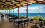 Überdachte Außenterrasse mit dunklen Holztischen und herrlichem Blick auf das tiefblaue Meer.