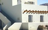 Traditionell weißes Gebäude mit typischer kykladischer Architektur und gemütlichem Sitzbereich am glitzernden Pool – perfekter Ort zum Entspannen unter der Sonne Santorins.