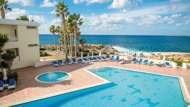 Großer Außenpool mit integriertem Kinderbecken und Meerblick, umgeben von Liegestühlen und Palmen.