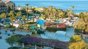 Großzügige Hotelanlage mit mehreren Pools, Palmen, weißen Sonnenschirmen und Meerblick – eine mediterrane Oase zum Entspannen.