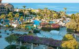 Großzügige Hotelanlage mit mehreren Pools, Palmen, weißen Sonnenschirmen und Meerblick – eine mediterrane Oase zum Entspannen.