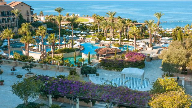 Großzügige Hotelanlage mit mehreren Pools, Palmen, weißen Sonnenschirmen und Meerblick – eine mediterrane Oase zum Entspannen.